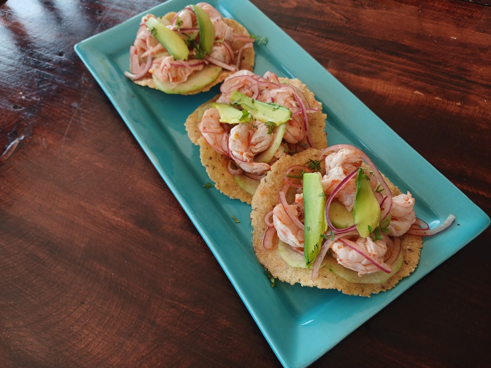 Tres tostadas de aguachile de camarón con pepino, cebolla morada y aguacate sobre un plato turquesa